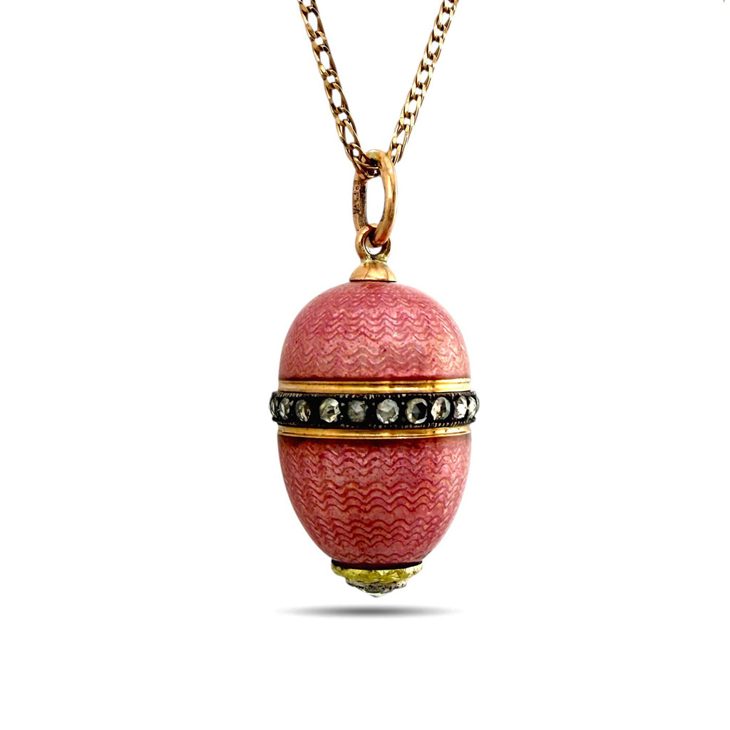 Pink enamel egg charm pendant with gold tone ring top, stone band, and chain necklace.