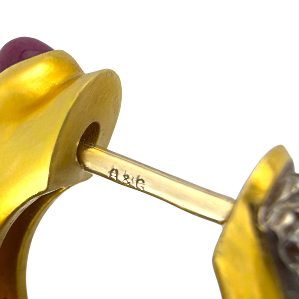 Close-up of an earring post stamped 18K beside a ruby-set gold clasp