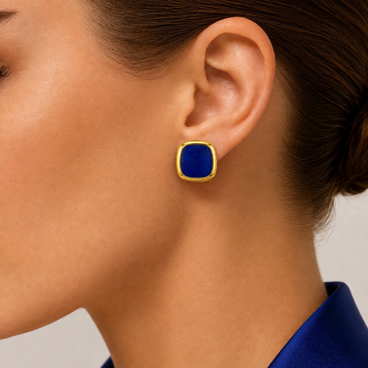 Gold lapis lazuli stud earring on ear, featuring a square blue gemstone bezel