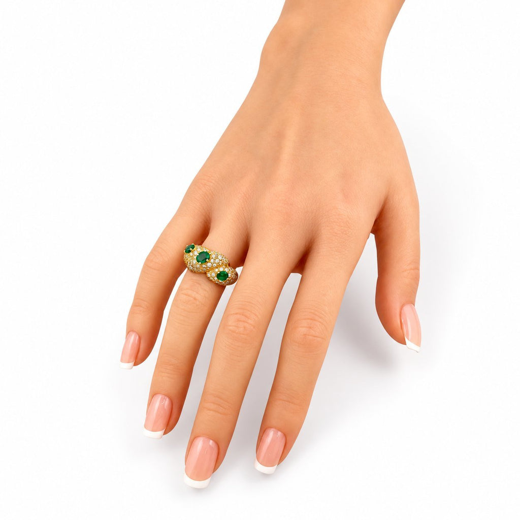 Gold emerald and diamond ring on hand, green gemstones surrounded by white diamonds