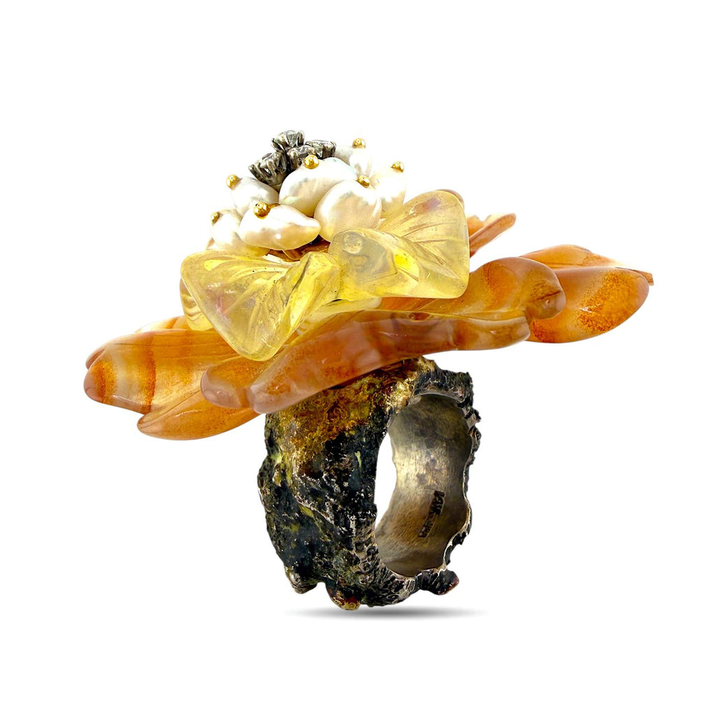 Orange flower ring with pearl-like cluster, translucent petals, and dark metal band