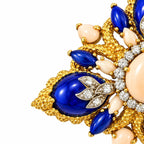 Close-up gold-tone brooch with blue enamel drops, white stones, and oval pale center