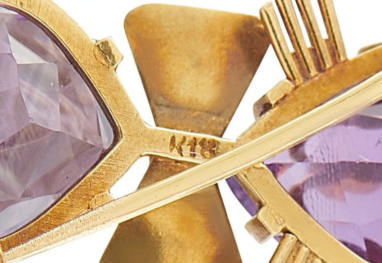 Gold cat brooch close-up with purple gemstone prongs and bar details