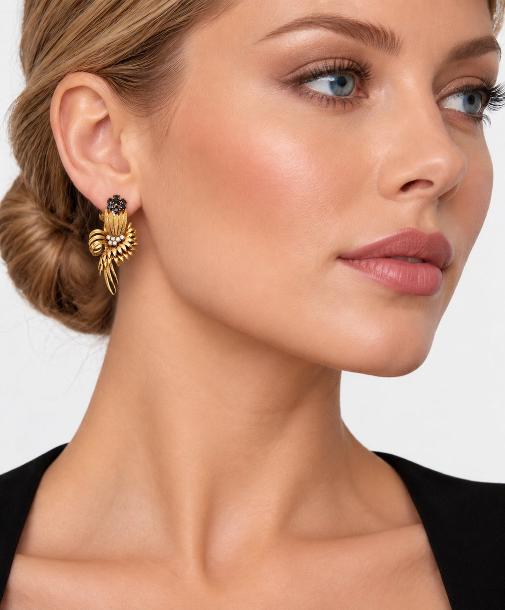 Gold fan earring with dark blue stones and diamond accents on model ear
