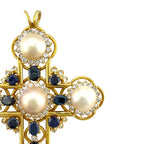 Gold cross pendant close-up with pearls, dark blue sapphires, and diamond settings