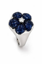 Three-quarter view of blue sapphire flower ring with round diamond center in white gold