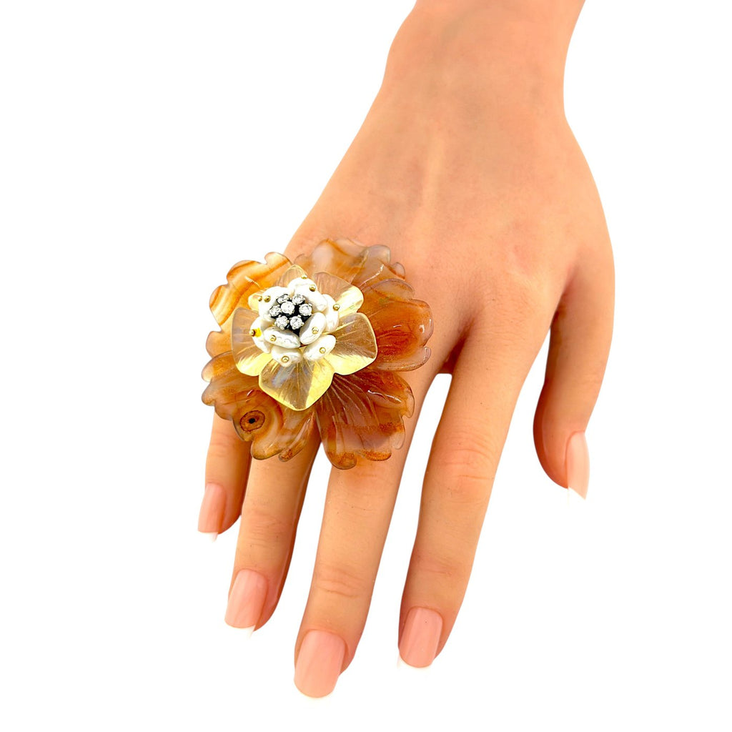 Flower ring worn on finger with amber petals and pearl-like center with sparkling stones