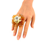 Flower ring worn on finger with amber petals and pearl-like center with sparkling stones