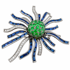 Gemstone brooch with round green center, blue sapphire baguette rays, and diamond detailing