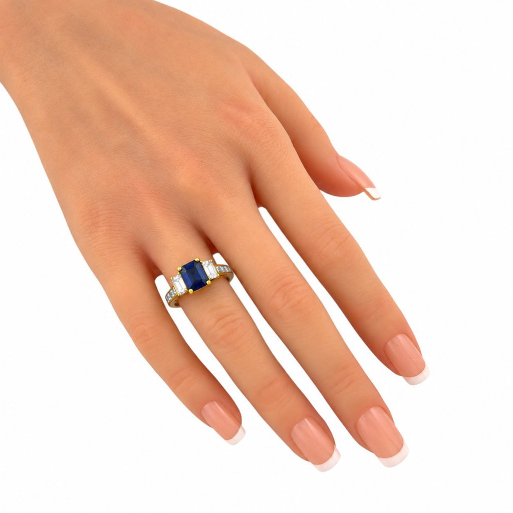 18K yellow gold ring on finger with blue sapphire center and baguette diamond stones