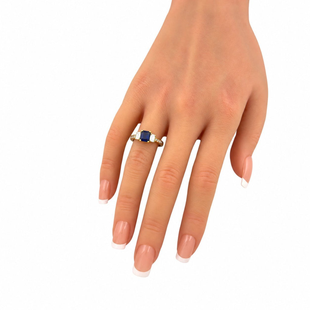 18K yellow gold ring on hand with blue sapphire center and baguette diamond stones