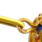 Close-up of a gold cufflink joint with engraved detail and a blue sapphire