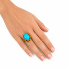 Turquoise cabochon ring on hand, with gold beaded halo and prong setting