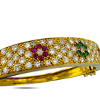 Close-up of yellow gold diamond pave cuff with ruby, blue, and green gemstone details