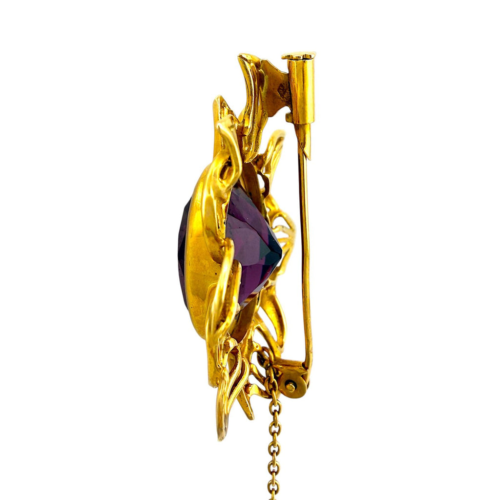 Side view of gold sunburst brooch with dark amethyst center and clasp