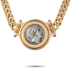 Gold tone round coin pendant with engraved profile and small purple/red side stones