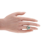 Platinum cluster ring with green emerald center and diamond halo on hand