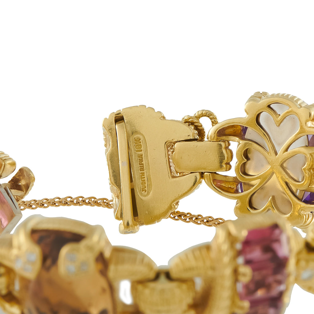 Gold bracelet clasp close-up with heart motif and faceted pink and blue stones