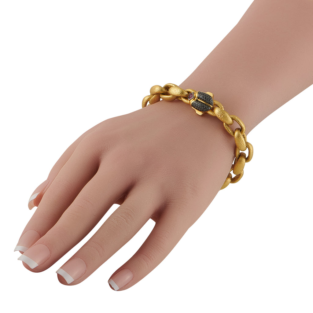Yellow gold chain bracelet on wrist with small dark and red gemstone details