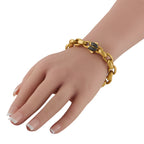 Yellow gold chain bracelet on wrist with small dark and red gemstone details