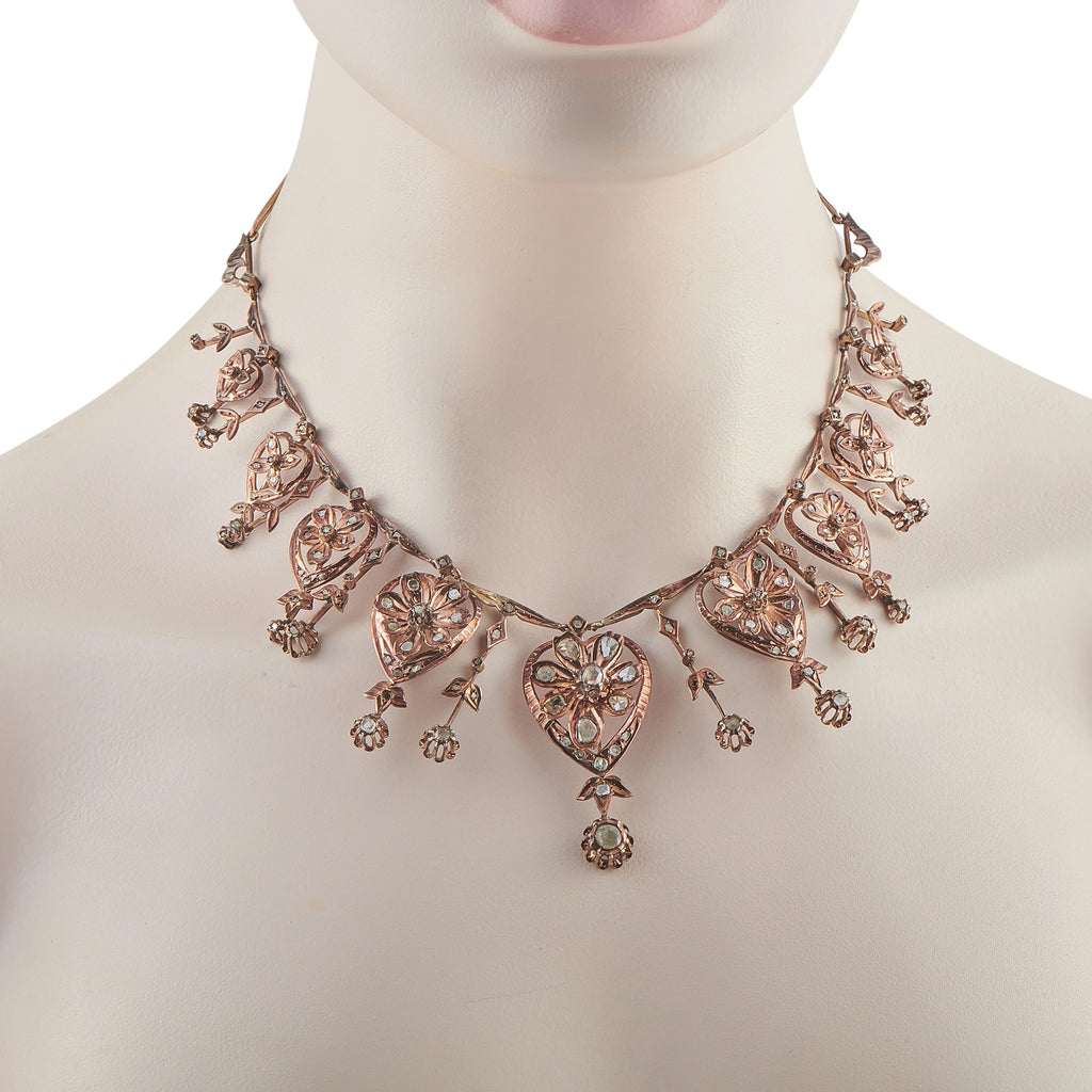 Rose gold diamond necklace on model with heart stations and floral fringe, V-shape