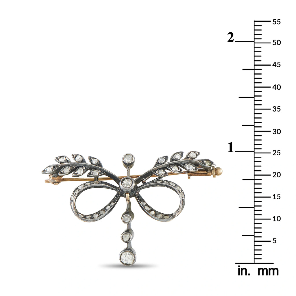 Diamond bow brooch on measuring scale, ornate loops and dangling round stone