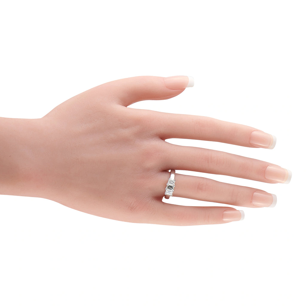 14K white gold three-stone diamond ring worn on hand, emerald-cut center stone