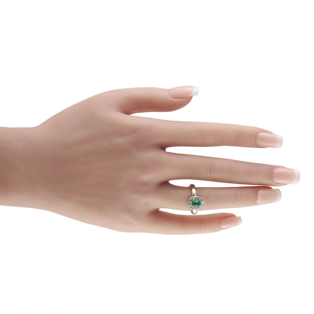White gold ring with green emerald and diamond halo worn on finger