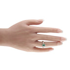 White gold ring with green emerald and diamond halo worn on finger