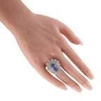 Platinum diamond and sapphire ring worn on a hand, with a pear-shaped blue center stone.