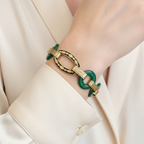 Gold and green bracelet on a wrist with a beige background
