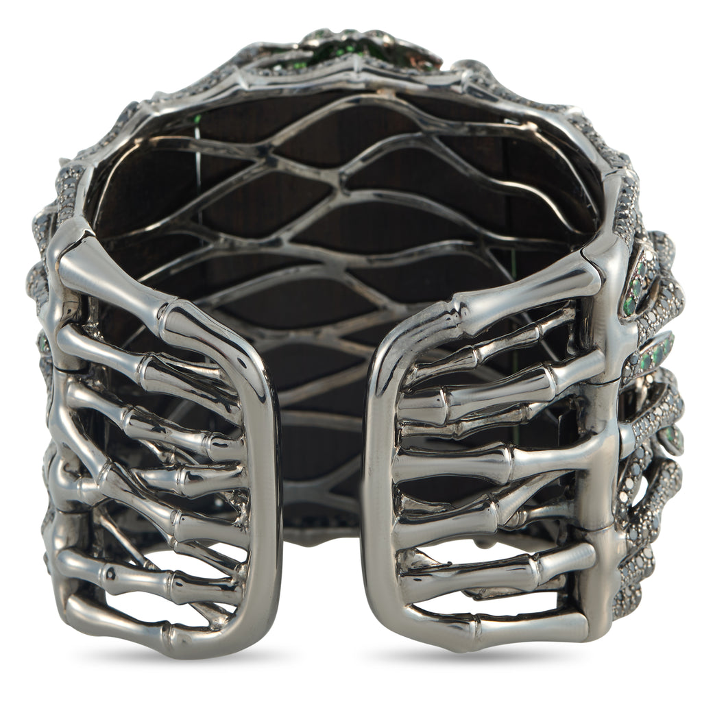 Openwork white gold cuff bracelet with dark interior backing and prong-set green accents