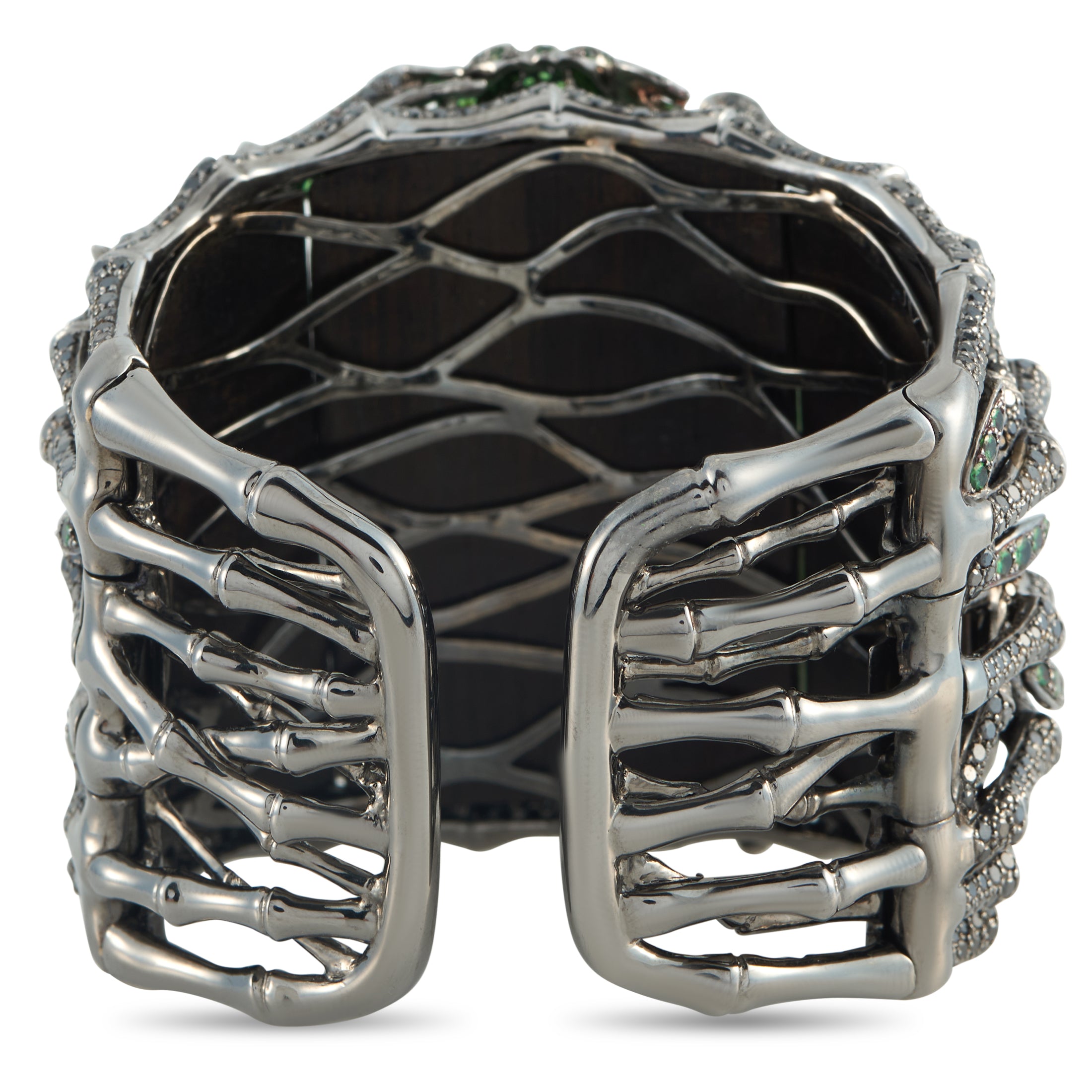 Openwork white gold cuff bracelet with dark interior backing and prong-set green accents
