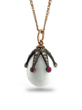 Gold egg pendant on a chain with dark metal setting and red ruby cabochons