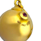 Close-up of 18K yellow gold ball earring with purple gemstone detail on top