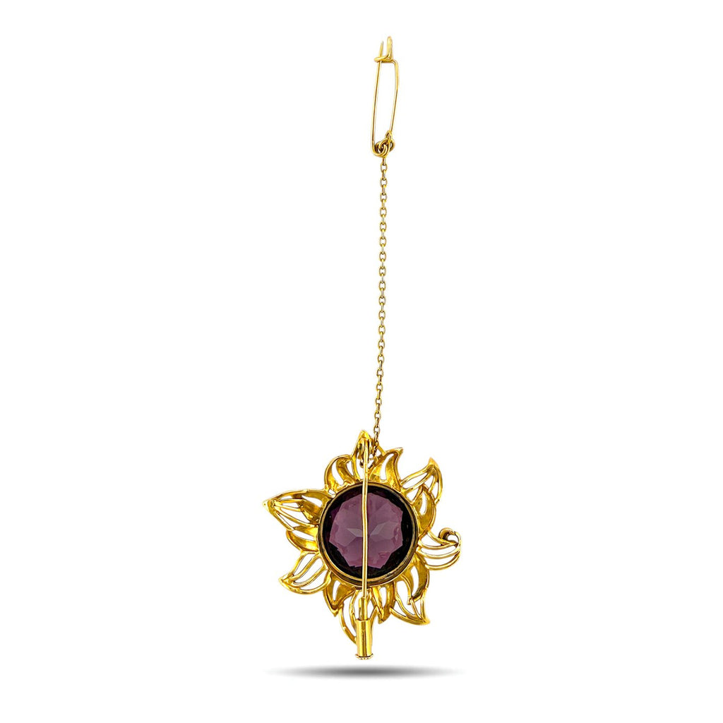Gold sunburst brooch with round dark amethyst center on a slender chain