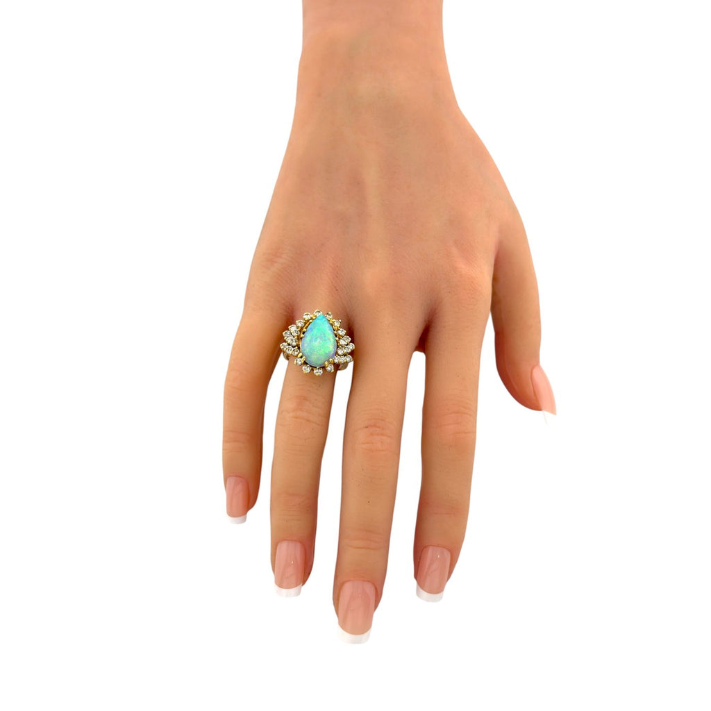 Hand model wearing a pear opal ring with diamond halo in 14k yellow gold