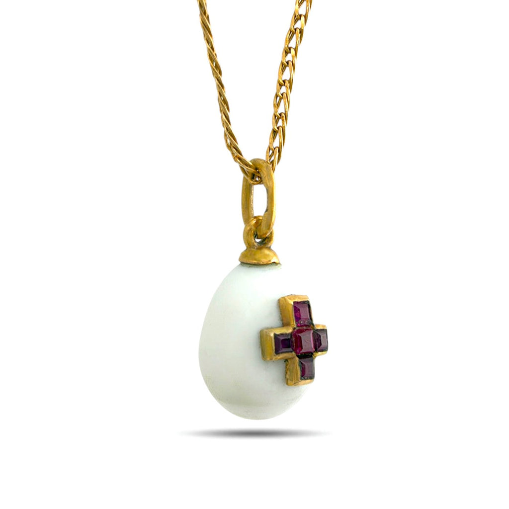 Side view of white egg pendant with a gold-tone ruby cross and chain