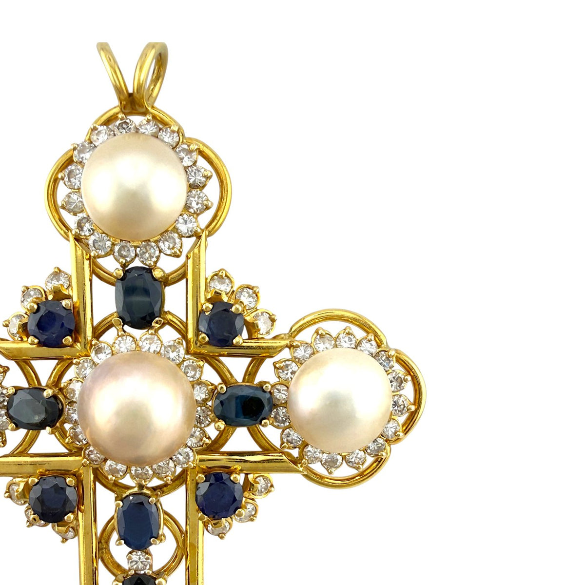 Close-up gold cross pendant detail with pearls, blue sapphires, and diamond borders