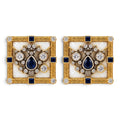 Two square gold cufflinks with blue center stone, halo of clear gems, and black accents